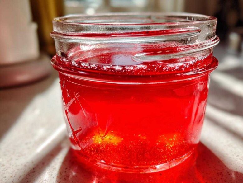 Close-up of bright red Homemade Strawberry Lemonade Concentrate stored in a glass mason jar.