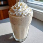 Close-up of a tall glass filled with a speckled Homemade Vanilla Bean Frappuccino topped high with whipped cream.