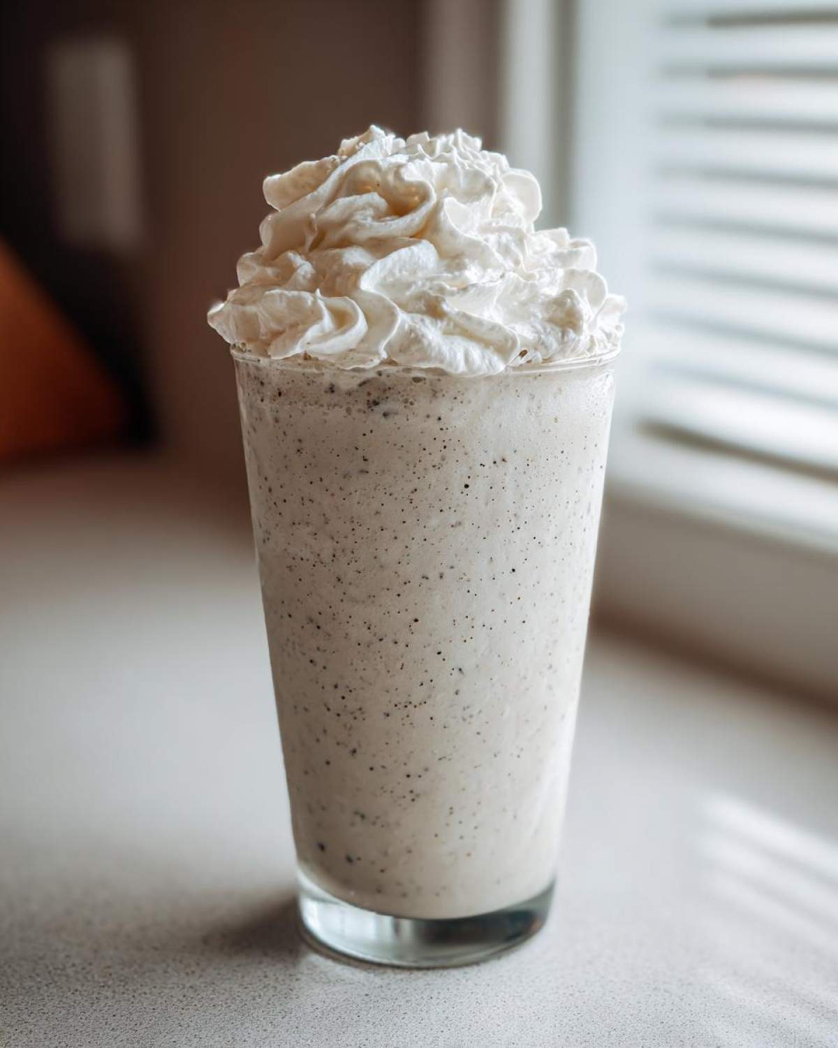 A tall glass of Homemade Vanilla Bean Frappuccino topped generously with whipped cream.