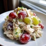 A mound of creamy Honey Mustard Chicken Salad with Grapes, featuring shredded chicken, red and green grapes, and celery.