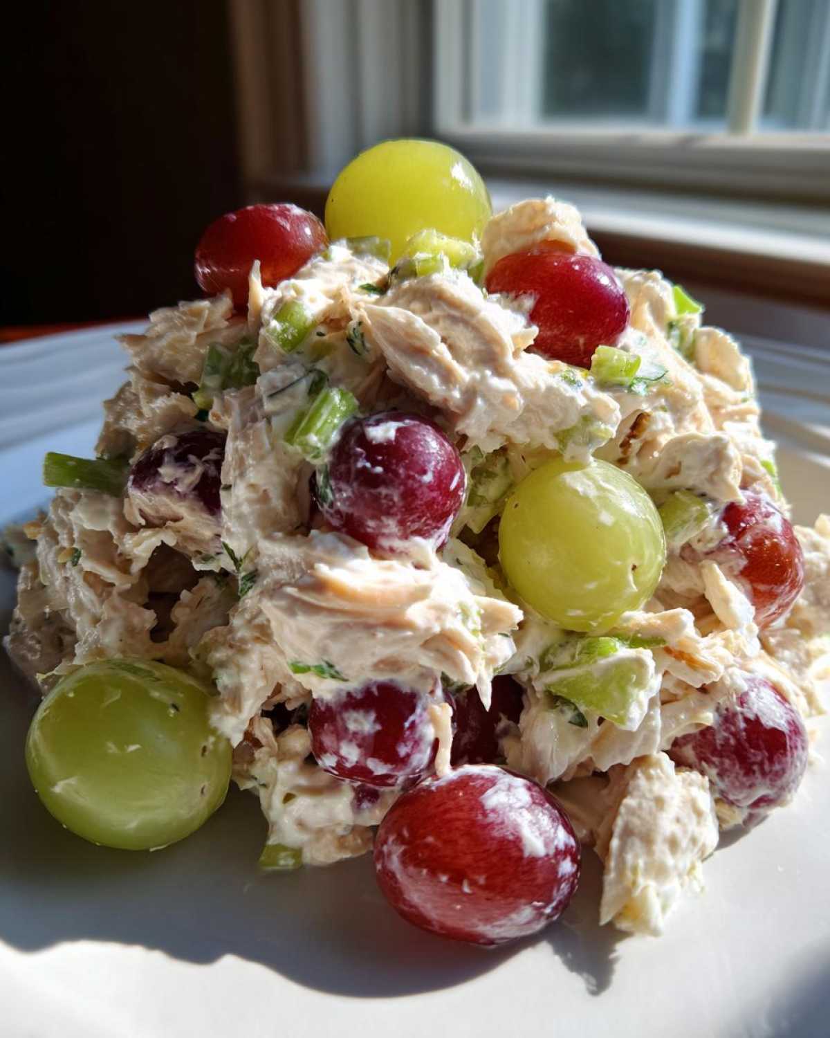 A mound of creamy Honey Mustard Chicken Salad with Grapes, featuring shredded chicken, celery, and whole red and green grapes.