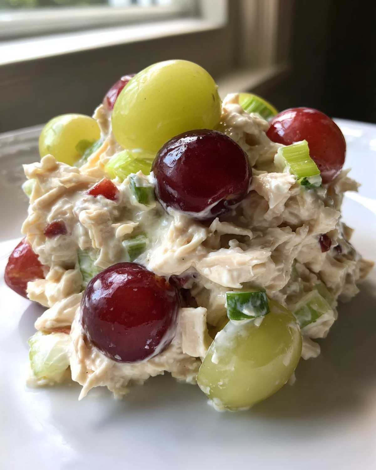 A scoop of creamy Honey Mustard Chicken Salad with Grapes, celery, and red grape halves on a white plate.