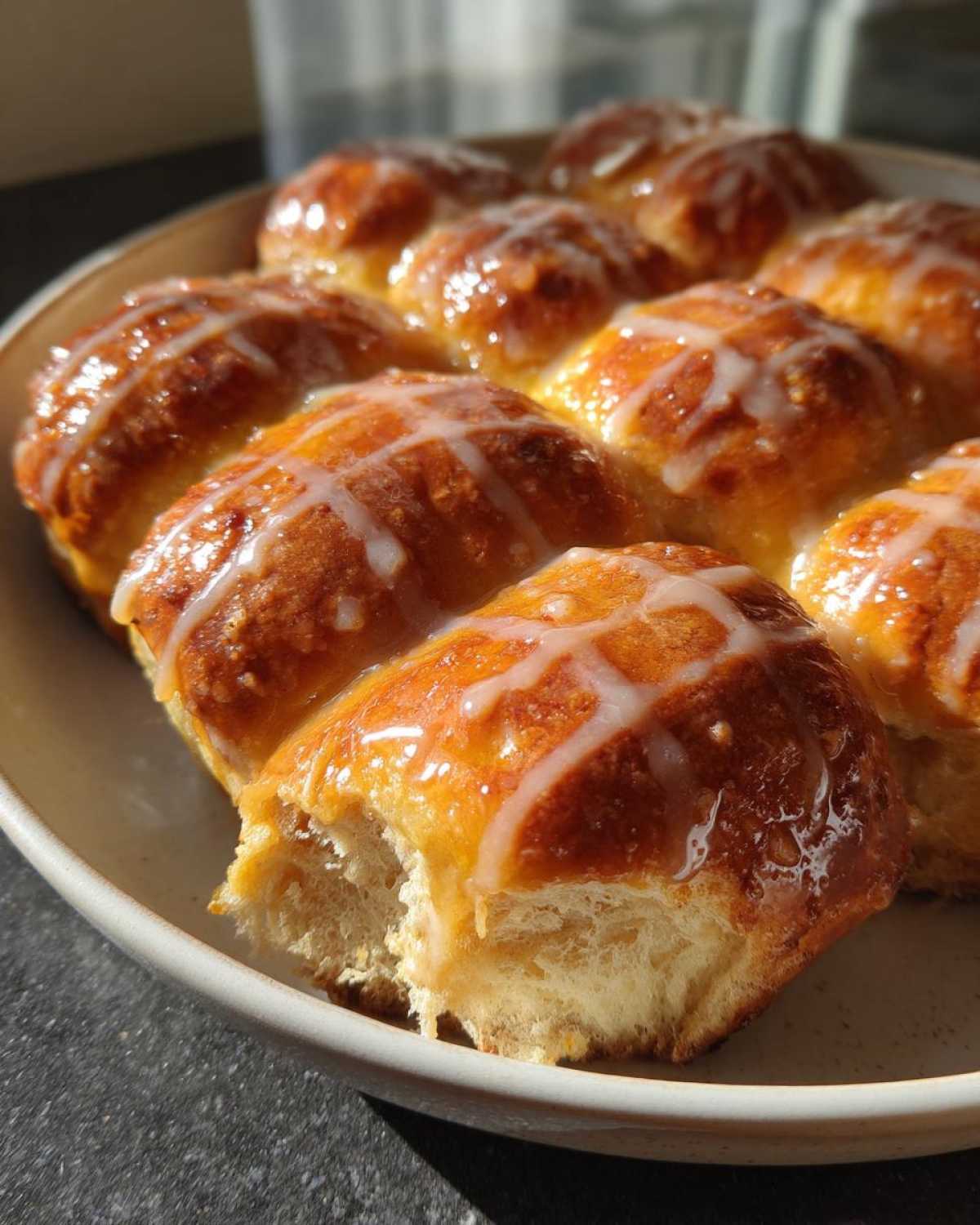 A plate of freshly baked Hot Cross Buns with Orange Glaze, featuring a shiny glaze and white icing crosses.