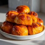 A tempting stack of freshly baked Hot Cross Buns with Orange Glaze piled high on a white plate.