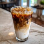 Close-up of a tall glass containing a beautiful Iced Caramel Macchiato with milk, espresso, and ice.