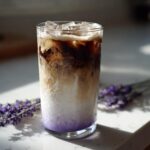 A tall glass of Iced Lavender Latte showing distinct layers of purple syrup, milk, and dark espresso, garnished with ice.