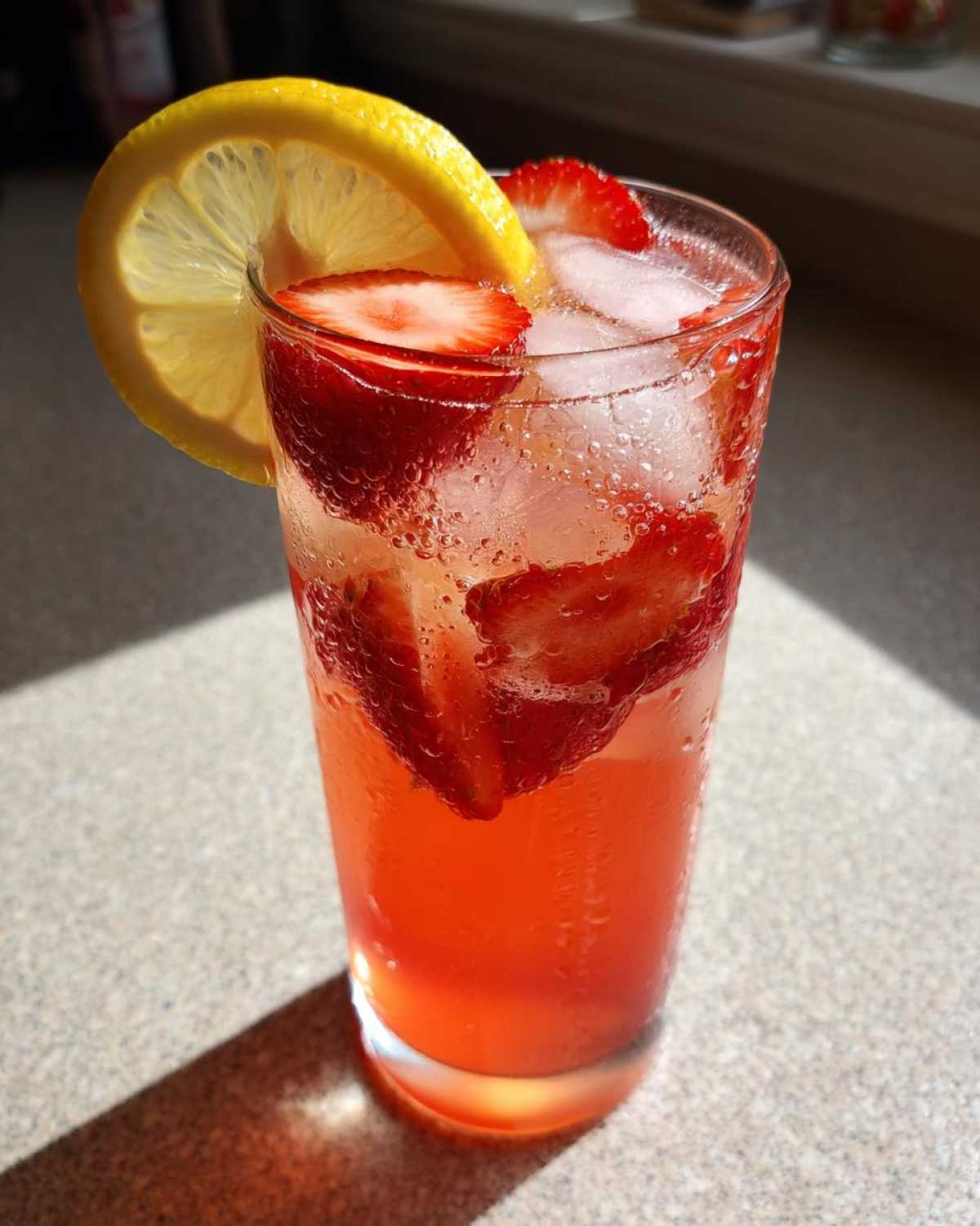 A tall glass filled with Iced Strawberry Lemon Tea, ice, sliced strawberries, and a lemon wheel garnish.