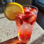 Close-up of a tall glass filled with Iced Strawberry Lemon Tea, featuring sliced strawberries and a lemon wheel garnish.