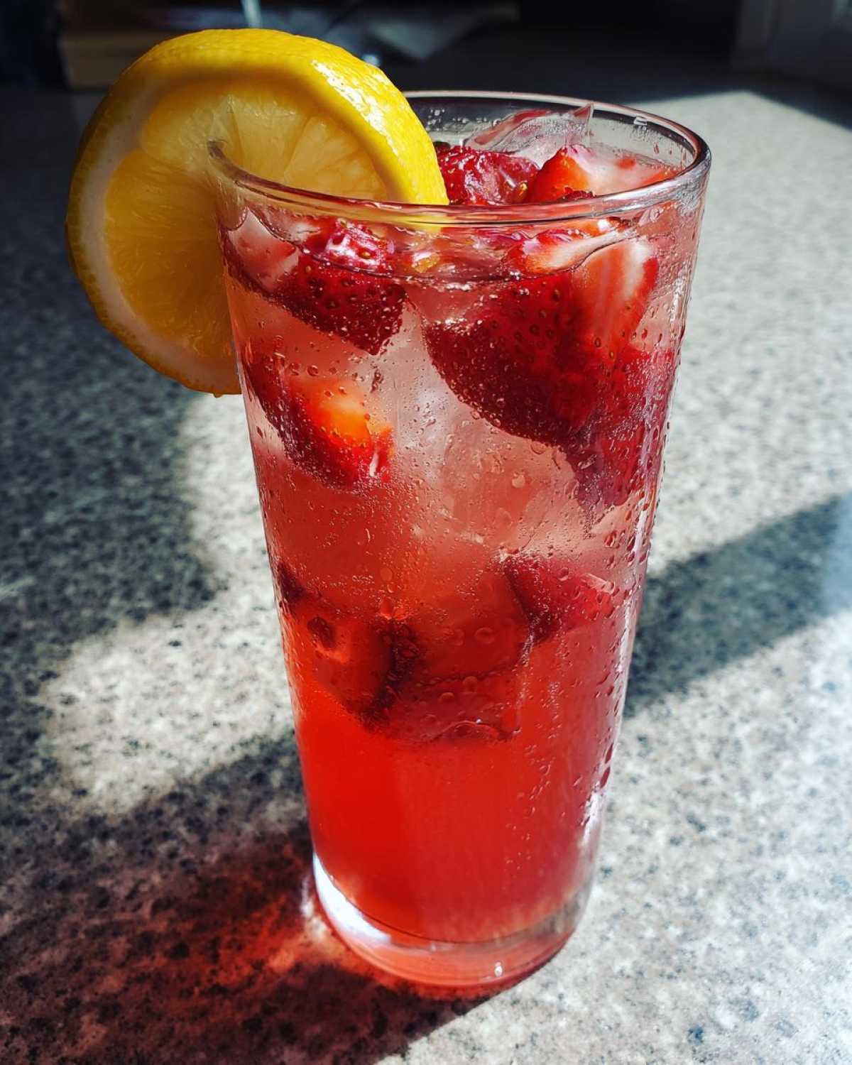 A tall glass filled with vibrant Iced Strawberry Lemon Tea, ice, sliced strawberries, and a lemon wheel garnish.