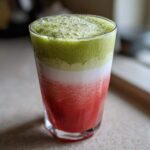Close-up of a layered Iced Strawberry Matcha Latte showing red strawberry puree, white milk, and green matcha foam.