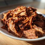 A mound of richly seasoned, shredded Instant Pot Beef Barbacoa piled high on a white plate.