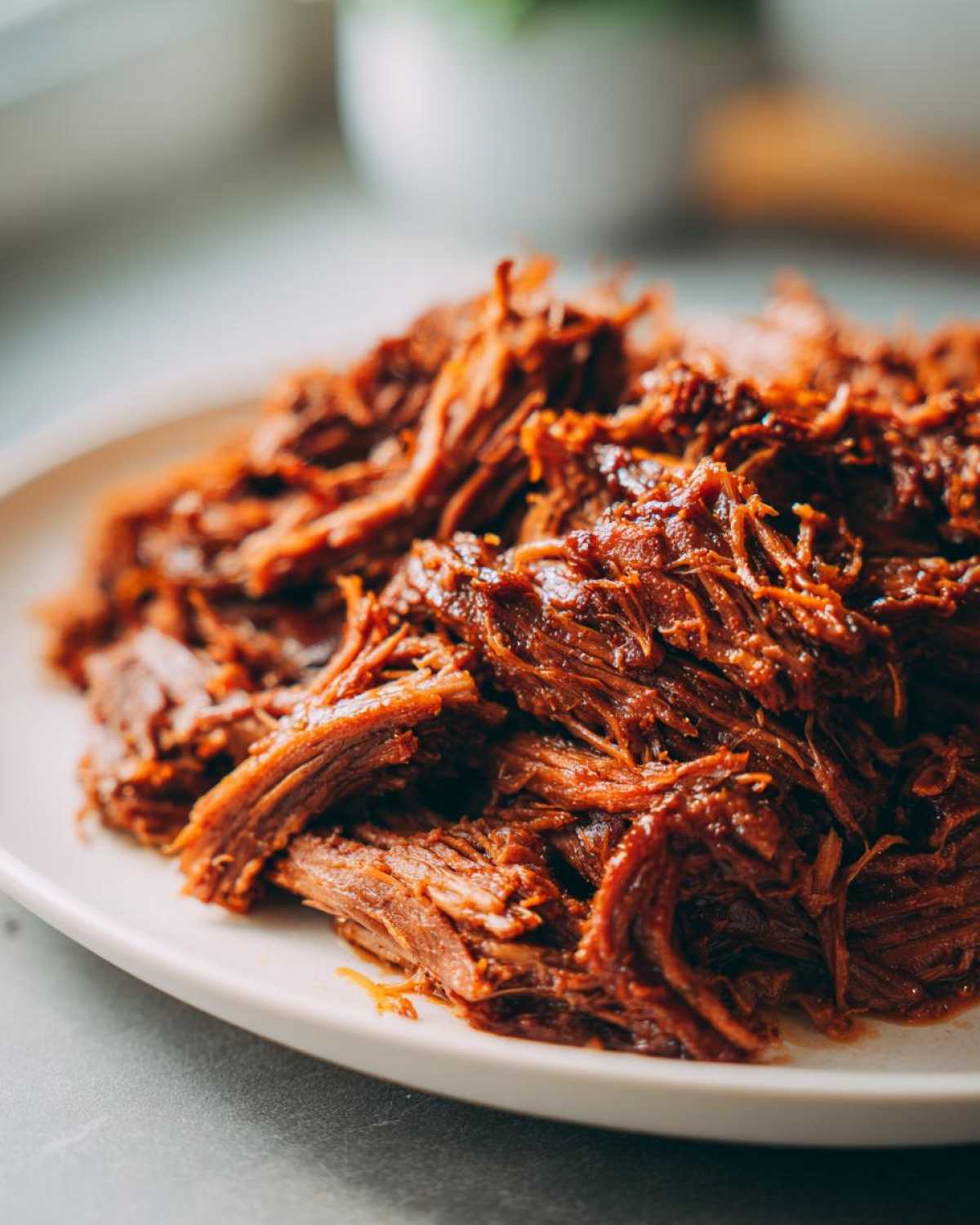 Close-up of richly seasoned, shredded Instant Pot Beef Barbacoa piled high on a white serving dish.