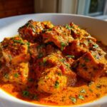 Close-up of tender chicken pieces coated in a rich, orange sauce, garnished with fresh cilantro, ready to eat Instant Pot Butter Chicken.