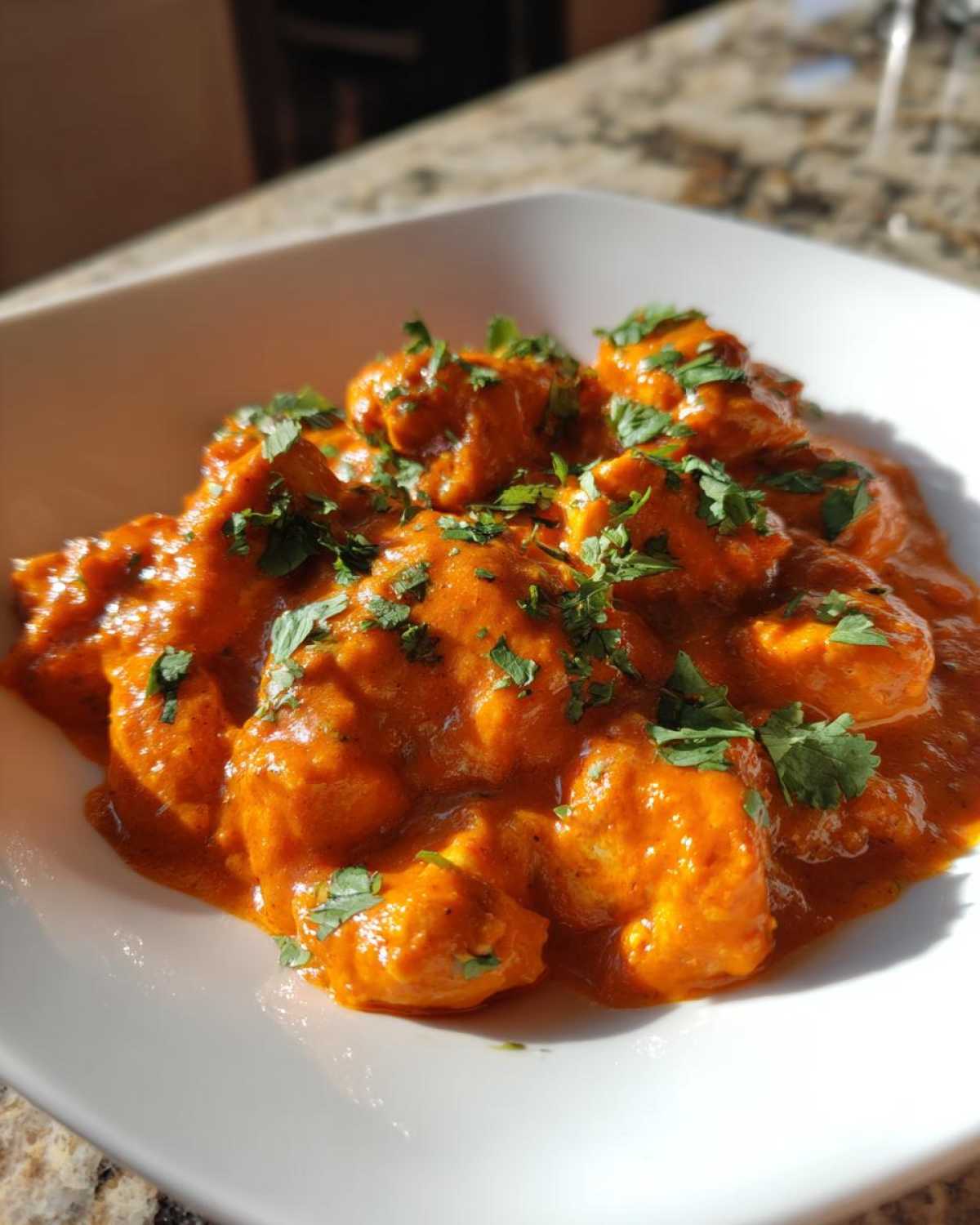Close-up of rich, orange-red Instant Pot Butter Chicken pieces garnished with fresh cilantro.