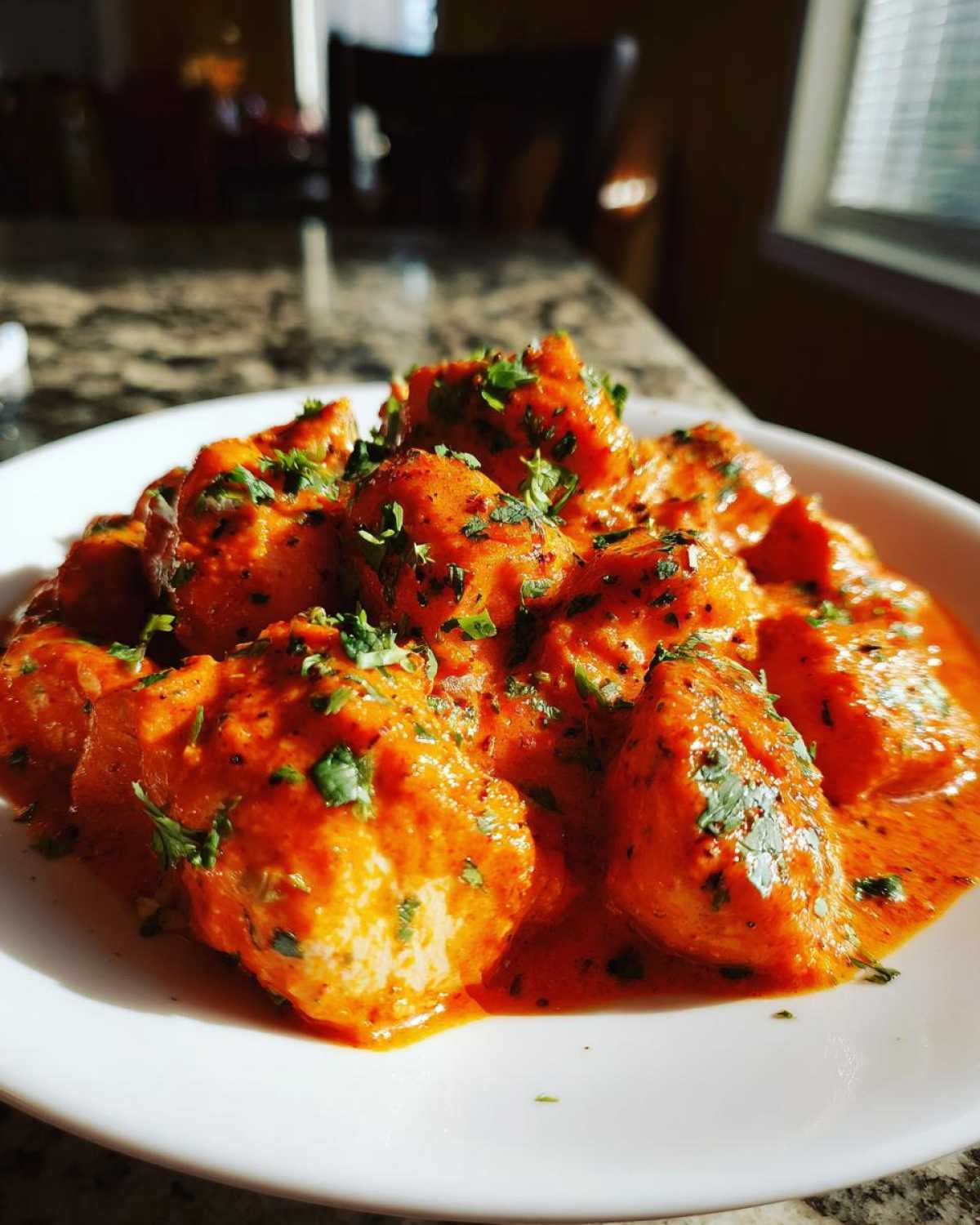 A close-up of tender chicken pieces coated in a vibrant orange, creamy sauce, garnished with fresh cilantro, representing Instant Pot Butter Chicken.