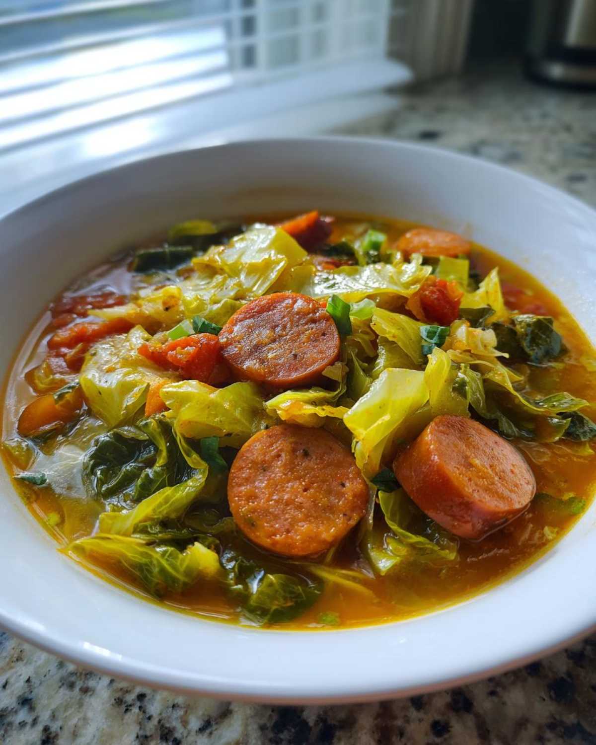 Close-up of a white bowl filled with Instant Pot Cabbage and Sausage Soup, featuring sliced sausage and cooked cabbage in broth.