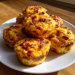 A stack of golden brown Keto Bacon and Egg Muffins with visible bacon pieces on a white plate.