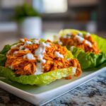 Close-up of Keto Buffalo Chicken Lettuce Wraps filled with shredded orange chicken and drizzled with white ranch dressing.