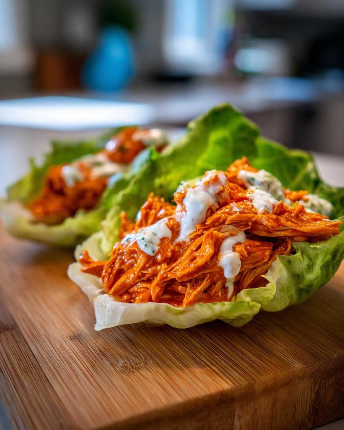 Two servings of Keto Buffalo Chicken Lettuce Wraps filled with shredded orange buffalo chicken and drizzled with ranch dressing.