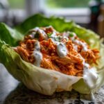 A single serving of Keto Buffalo Chicken Lettuce Wraps featuring shredded orange buffalo chicken topped with white ranch dressing.
