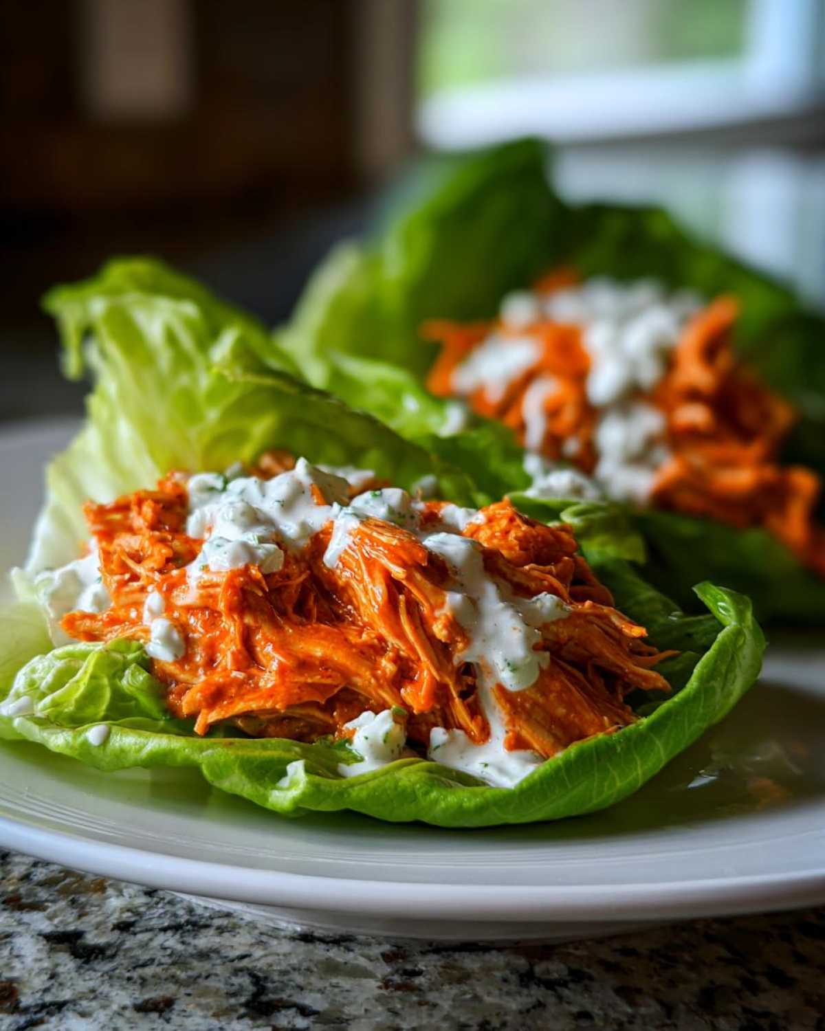 Two Keto Buffalo Chicken Lettuce Wraps filled with shredded orange buffalo chicken and drizzled with ranch dressing.