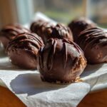 Close-up of several rich, chocolate-coated Keto Chocolate Peanut Butter Fat Bombs drizzled with extra chocolate.