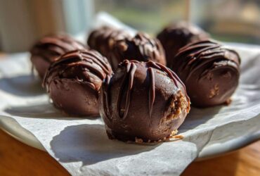 Close-up of several rich, chocolate-coated Keto Chocolate Peanut Butter Fat Bombs drizzled with extra chocolate.