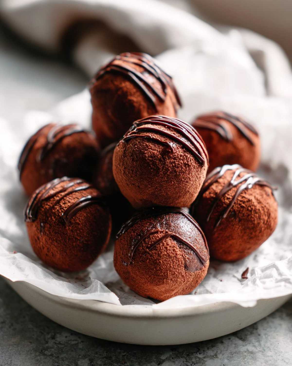A stack of rich, cocoa-dusted Keto Chocolate Peanut Butter Fat Bombs drizzled with dark chocolate.