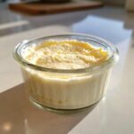 A single serving of fluffy Keto Lemon Cheesecake Mousse in a small glass ramekin, sitting on a white counter.