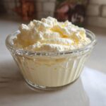 A serving of light yellow Keto Lemon Cheesecake Mousse topped with whipped cream in a small glass bowl.
