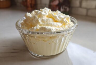 A serving of light yellow Keto Lemon Cheesecake Mousse topped with whipped cream in a small glass bowl.