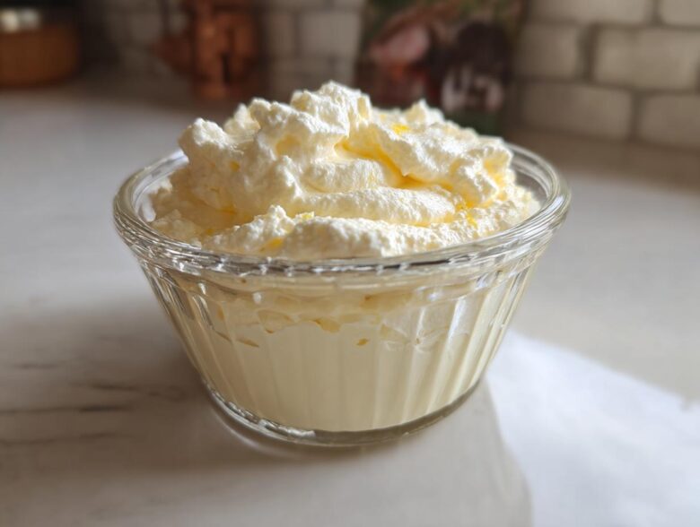 A serving of light yellow Keto Lemon Cheesecake Mousse topped with whipped cream in a small glass bowl.