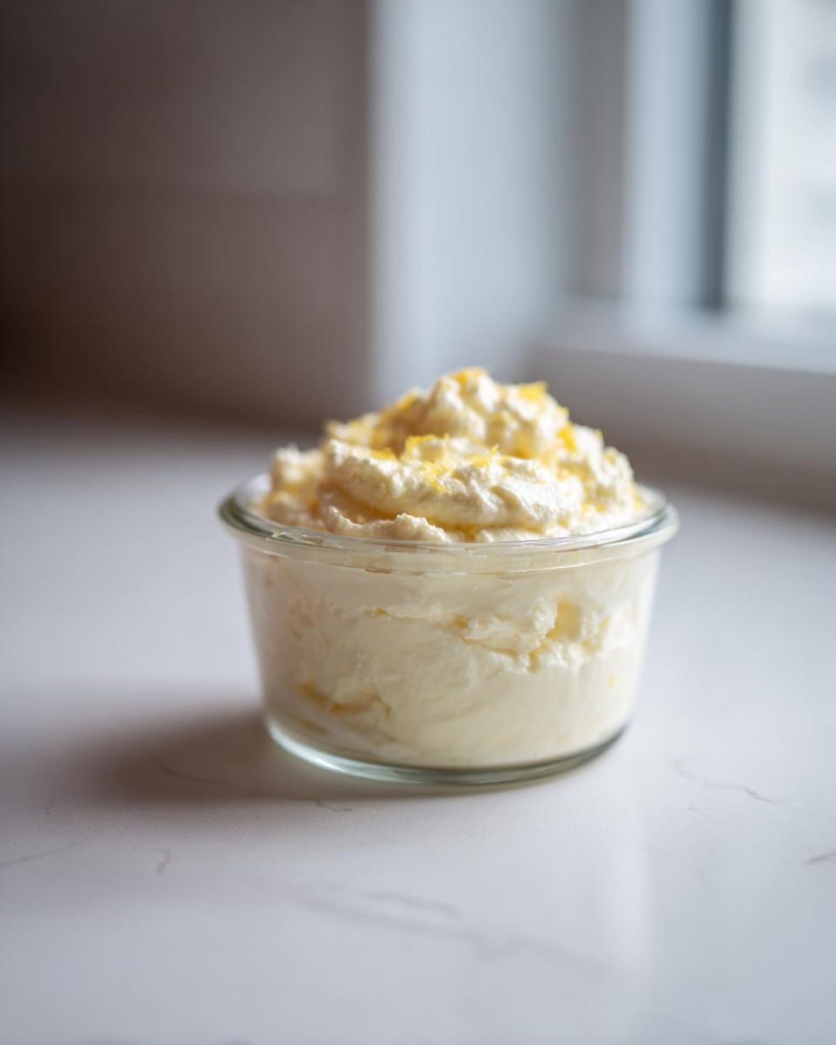 A single serving of fluffy Keto Lemon Cheesecake Mousse topped with lemon zest in a small glass jar.