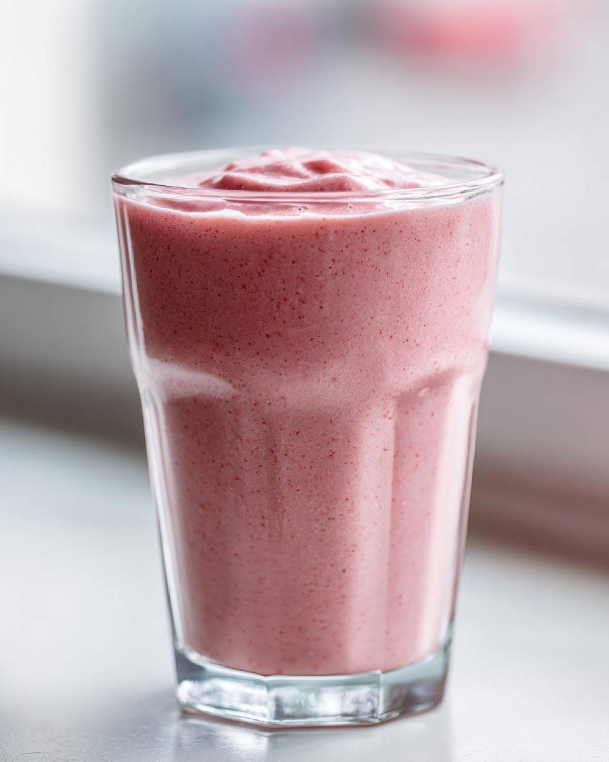 A close-up of a thick, pink Keto Strawberry Cheesecake Smoothie served in a clear glass.