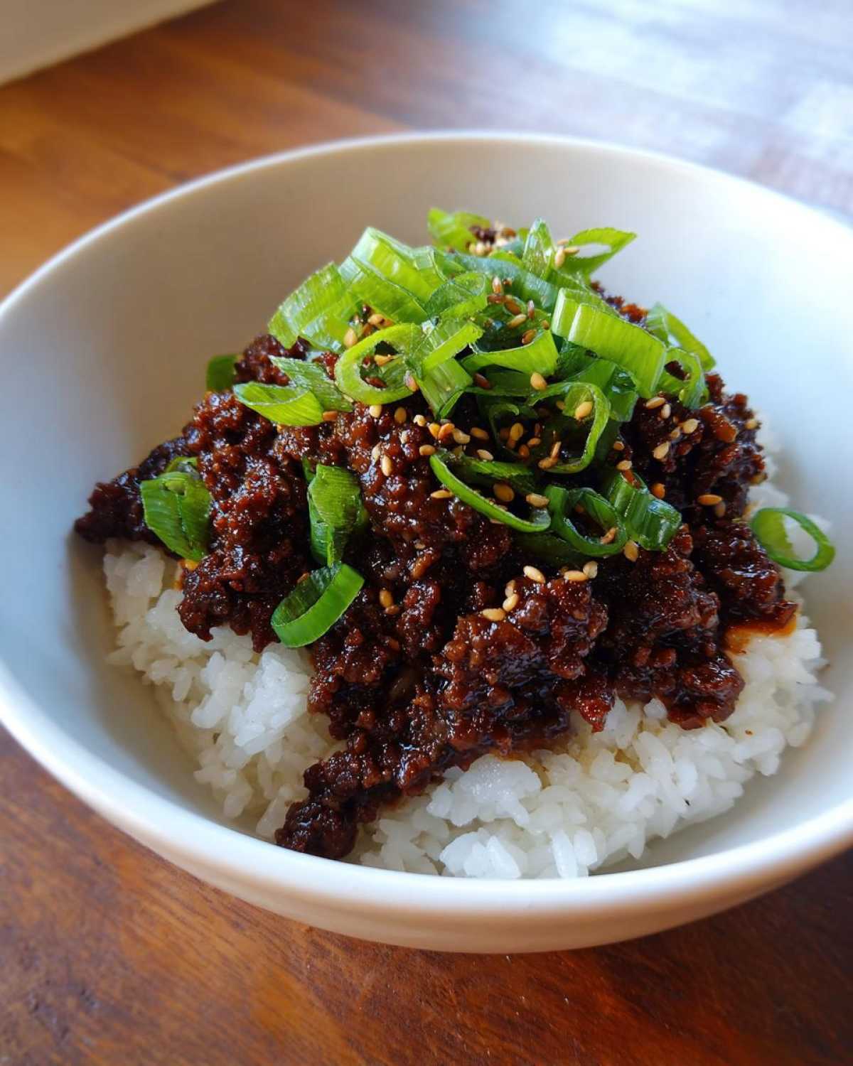 A close-up of Korean Ground Beef Bulgogi Bowls featuring savory ground beef over white rice, topped with sliced green onions and sesame seeds.