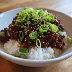 A close-up of a Korean Ground Beef Bulgogi Bowl featuring saucy ground beef over white rice, topped with sliced green onions and sesame seeds.