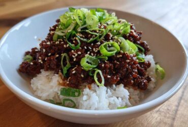 A close-up of a Korean Ground Beef Bulgogi Bowl featuring saucy ground beef over white rice, topped with sliced green onions and sesame seeds.