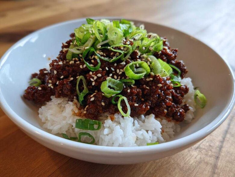 A close-up of a Korean Ground Beef Bulgogi Bowl featuring saucy ground beef over white rice, topped with sliced green onions and sesame seeds.