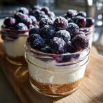 Close-up of individual Lemon Blueberry Cheesecake Jars featuring a graham cracker crust, creamy filling, and a topping of sugared blueberries.