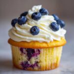 Close-up of a single Lemon Blueberry Cupcakes with Cream Cheese Frosting, topped with fresh blueberries.