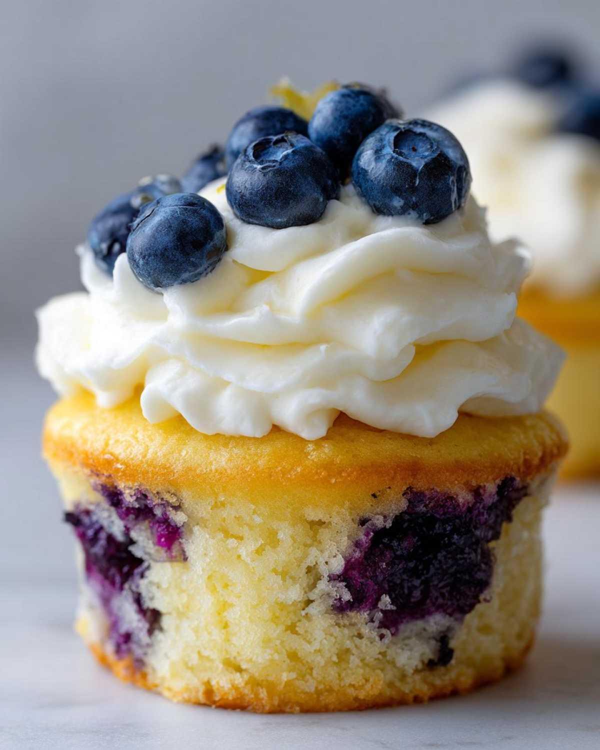 Close-up of a single Lemon Blueberry Cupcakes with Cream Cheese Frosting, topped with fresh blueberries.