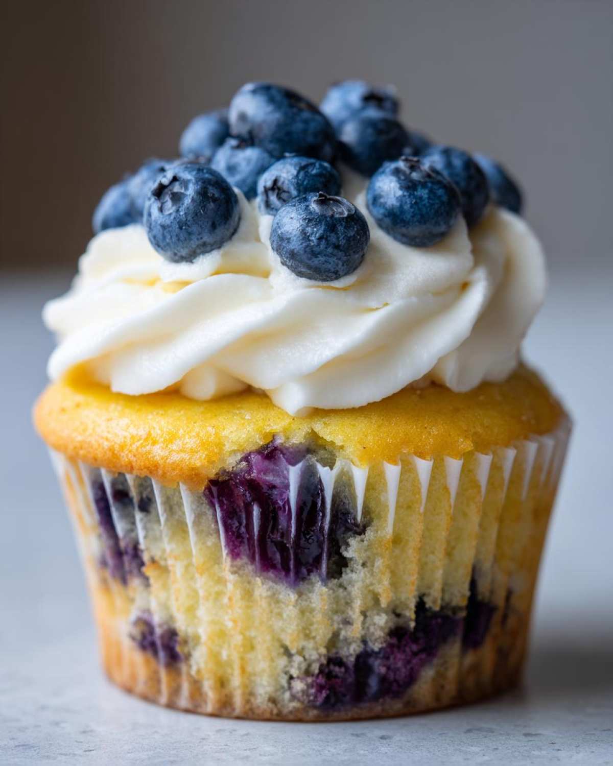 A single, moist Lemon Blueberry Cupcake topped with swirls of cream cheese frosting and fresh blueberries.
