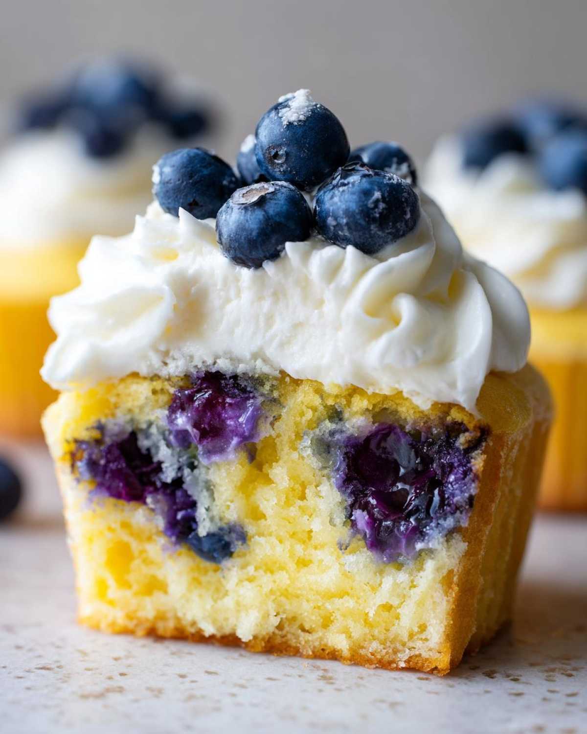 Close-up cross-section of a Lemon Blueberry Cupcakes with Cream Cheese Frosting, showing moist yellow cake and burst blueberries.