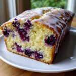 Close-up of a slice of Lemon Blueberry Yogurt Loaf showing moist crumb and thick white glaze.