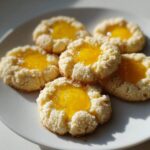 Five bright Lemon Curd Thumbprint Cookies with bright yellow filling piled on a white plate.