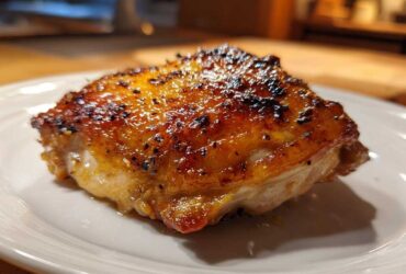 Close-up of a perfectly roasted Lemon Garlic Roasted Chicken Thighs with crispy, caramelized skin on a white plate.