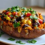 A close-up of a Loaded Veggie Stuffed Sweet Potato topped with black beans, corn, red peppers, melted cheese, and cilantro.