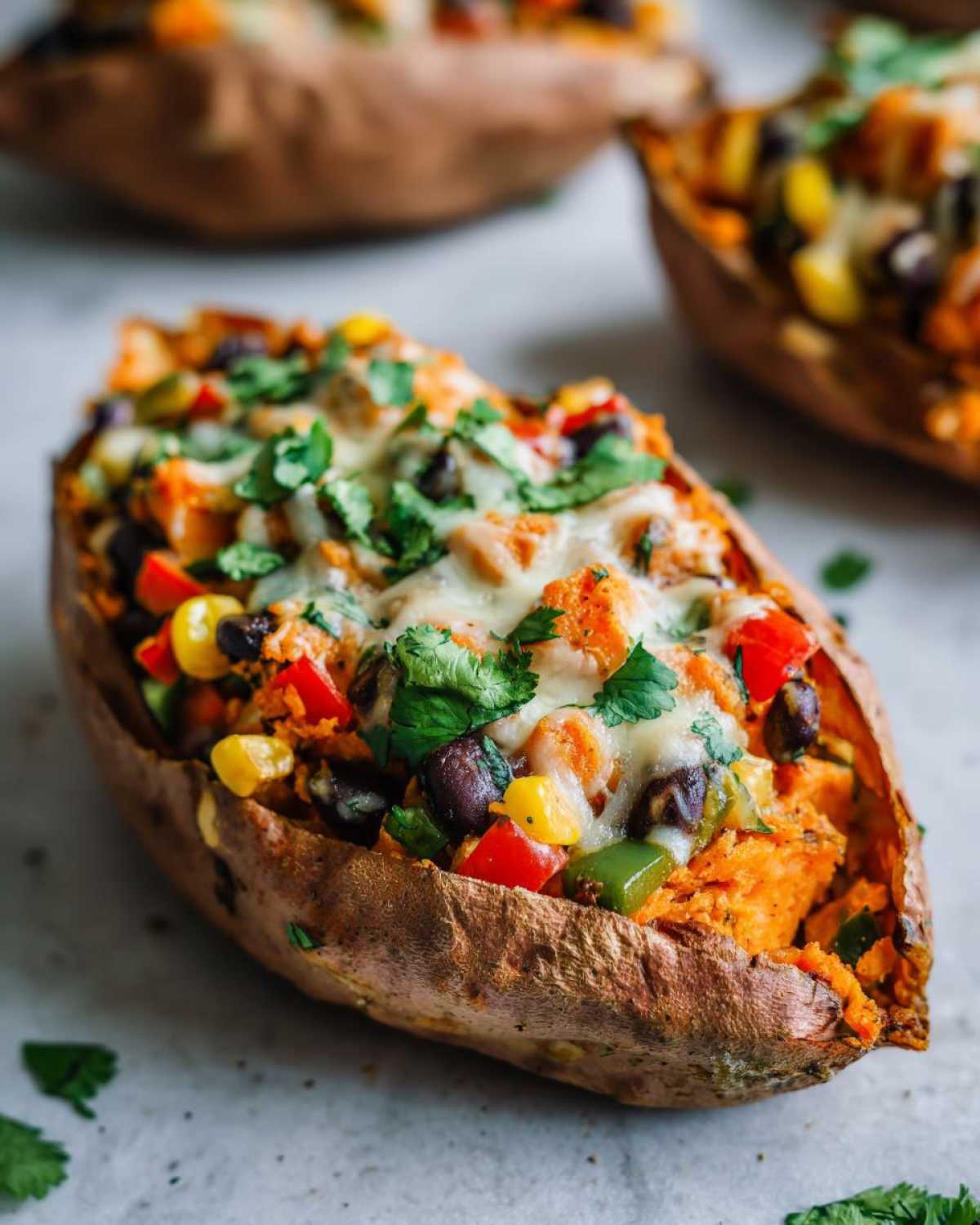 A close-up of a baked sweet potato split open and filled with a colorful mix for Loaded Veggie Stuffed Sweet Potatoes, topped with melted cheese and cilantro.