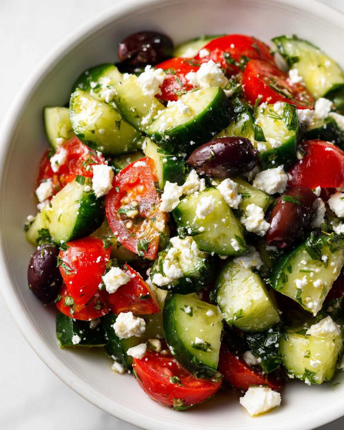 Close-up of a vibrant Mediterranean Cucumber Tomato Salad featuring chunks of cucumber, red tomatoes, feta cheese, and Kalamata olives.