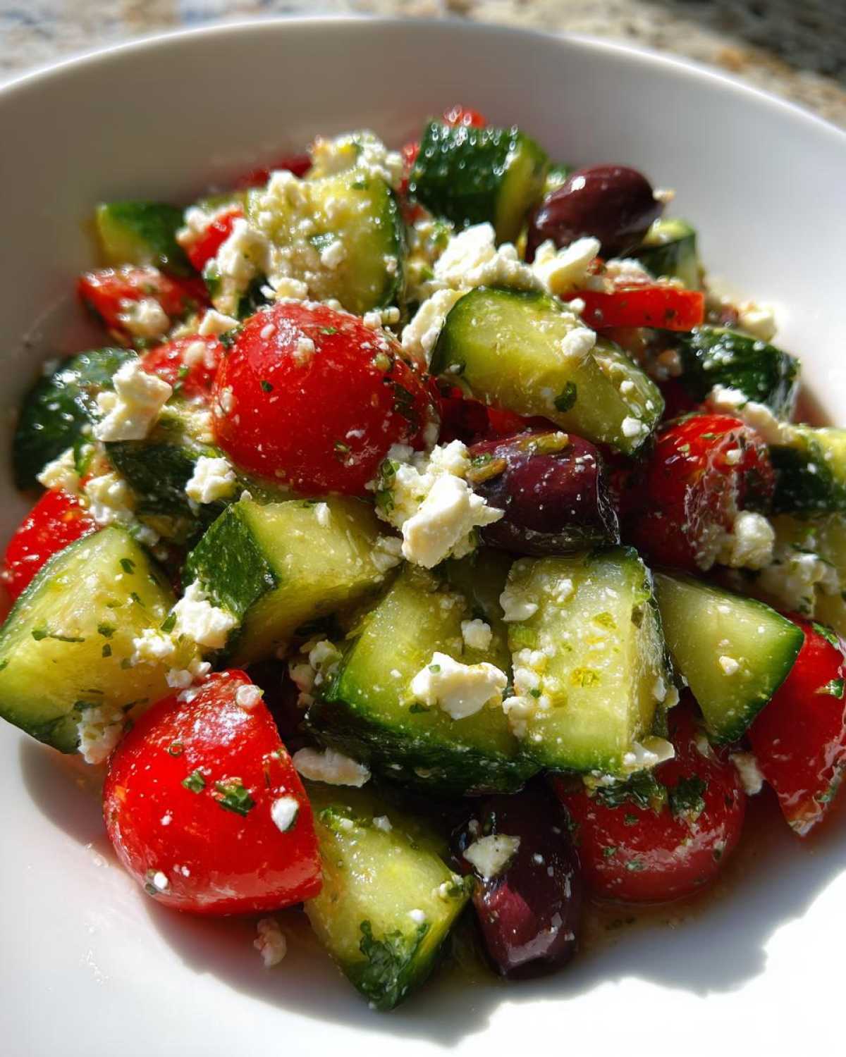 Vibrant close-up of Mediterranean Cucumber Tomato Salad with feta, olives, and herbs in a white bowl.